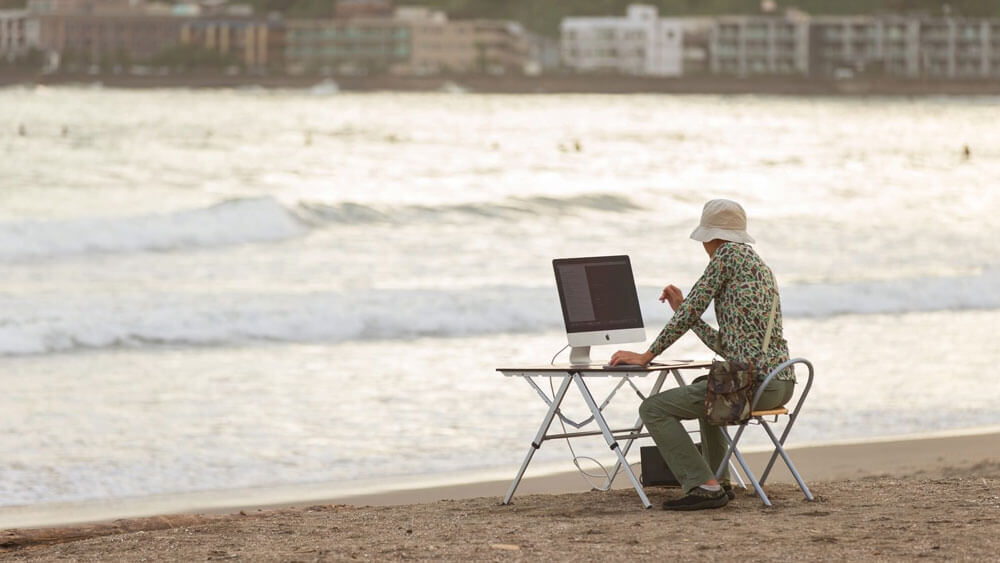 浜辺でパソコンを使う男